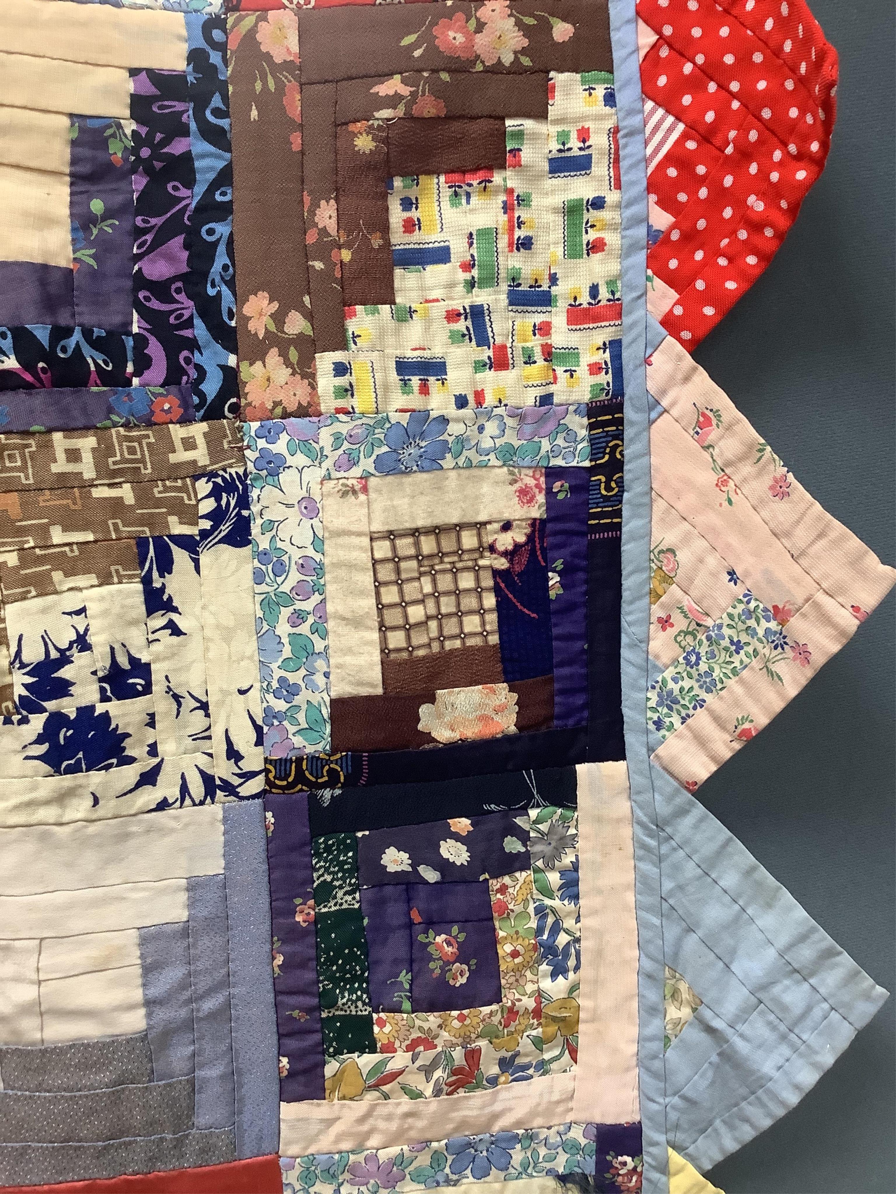 An early 20th century Log Cabin patchwork bedcover, worked in plain and printed silk, rayons and cottons from 1900 to 1940’s. Edged with a triangular patchwork border on three sides. Cover unlined. 158cm wide x 192cm lon